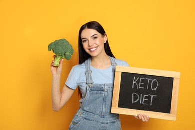 Photo of Happy woman holding broccoli and chalkboard with words Keto Diet on yellow background