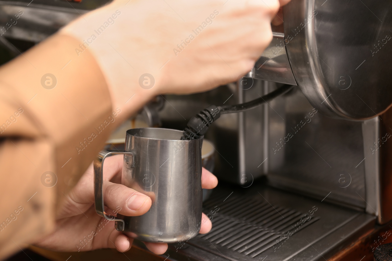 Photo of Barista steaming milk using coffee machine, closeup