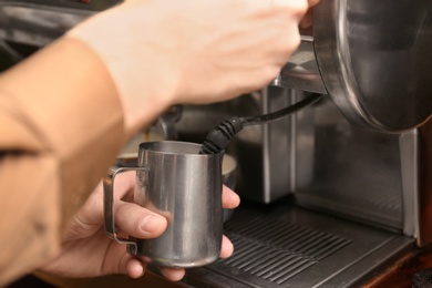 Photo of Barista steaming milk using coffee machine, closeup