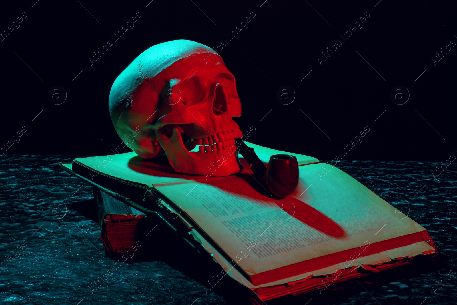 Photo of Human skull with smoking pipe and old book in neon lights on black background