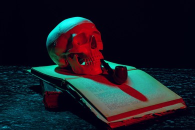 Human skull with smoking pipe and old book in neon lights on black background