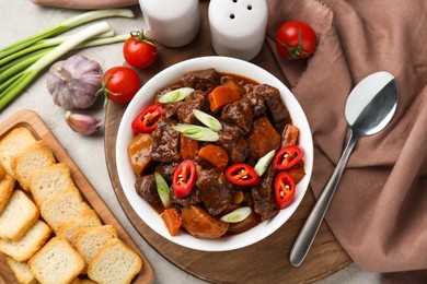 Delicious beef stew with carrots, chili peppers, green onions and potatoes served on white textured table, flat lay
