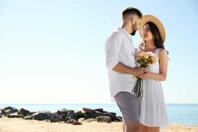 Happy young couple with flowers on beach near sea. Honeymoon trip