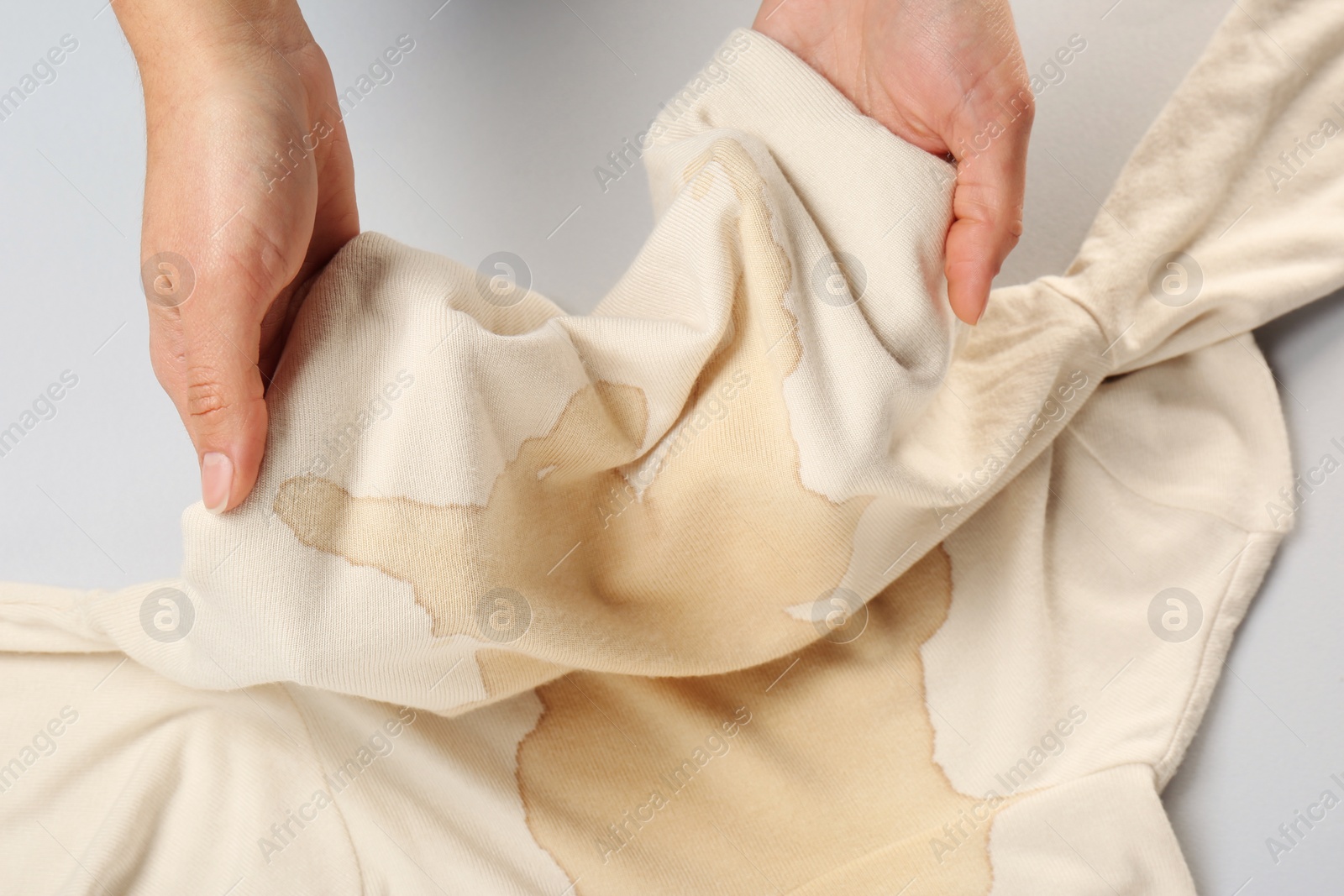 Photo of Woman holding beige sweater with stain on white background, closeup