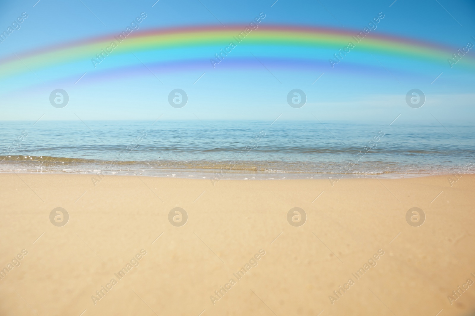 Image of Beautiful rainbow in blue sky over sandy beach and sea on sunny day