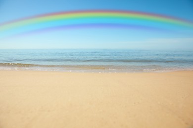 Image of Beautiful rainbow in blue sky over sandy beach and sea on sunny day