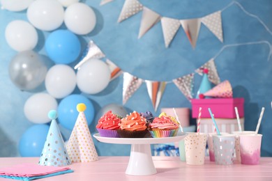 Photo of Different colorful cupcakes and party accessories on pink table