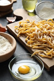 Photo of Board with homemade pasta, flour and ingredients on dark table