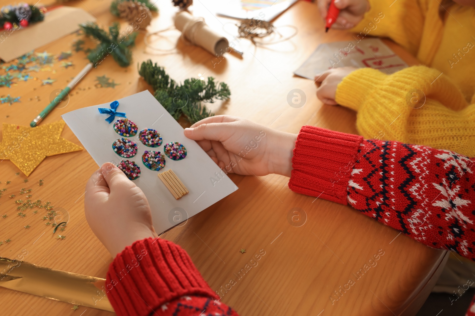 Photo of Little child with beautiful Christmas greeting card at wooden table, closeup