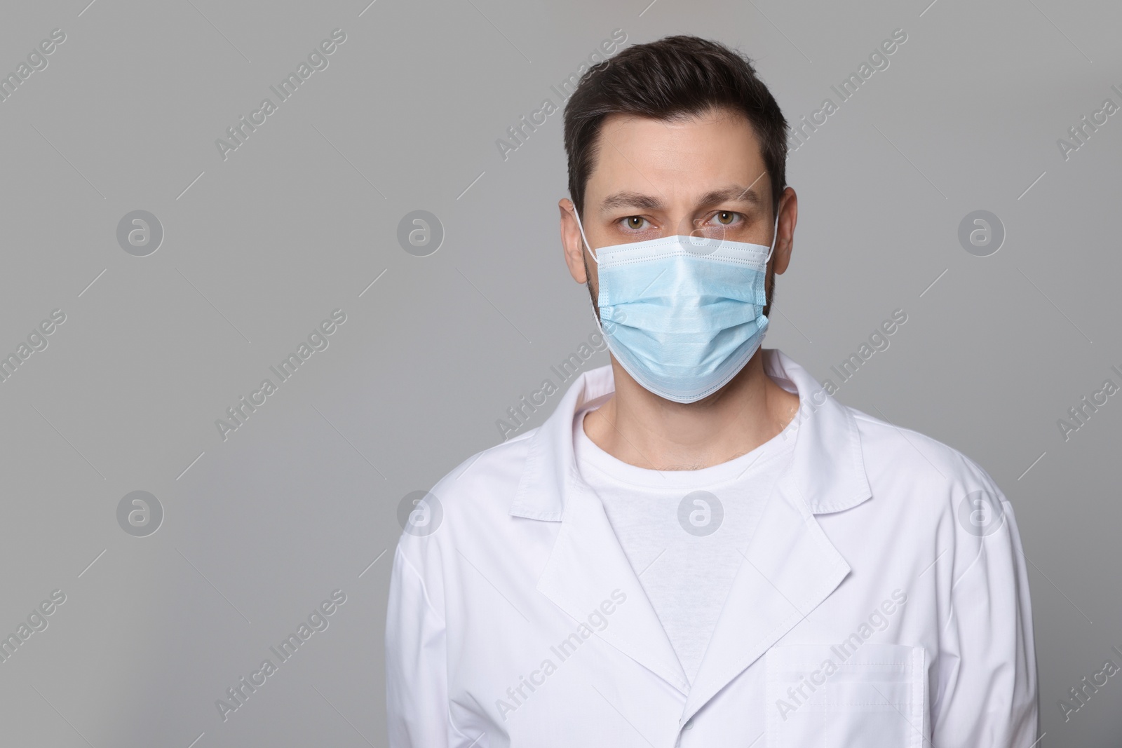 Photo of Doctor or medical assistant (male nurse) in uniform with protective mask on light grey background. Space for text