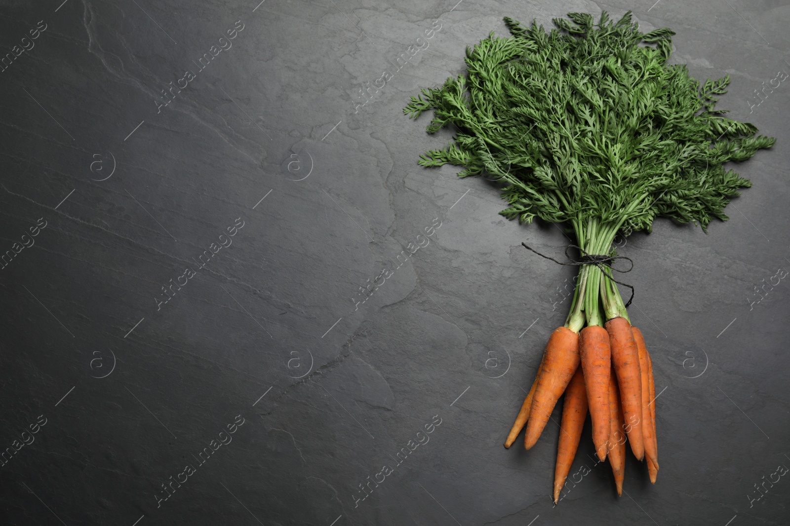 Photo of Bunch of tasty raw carrots on black slate table, top view. Space for text