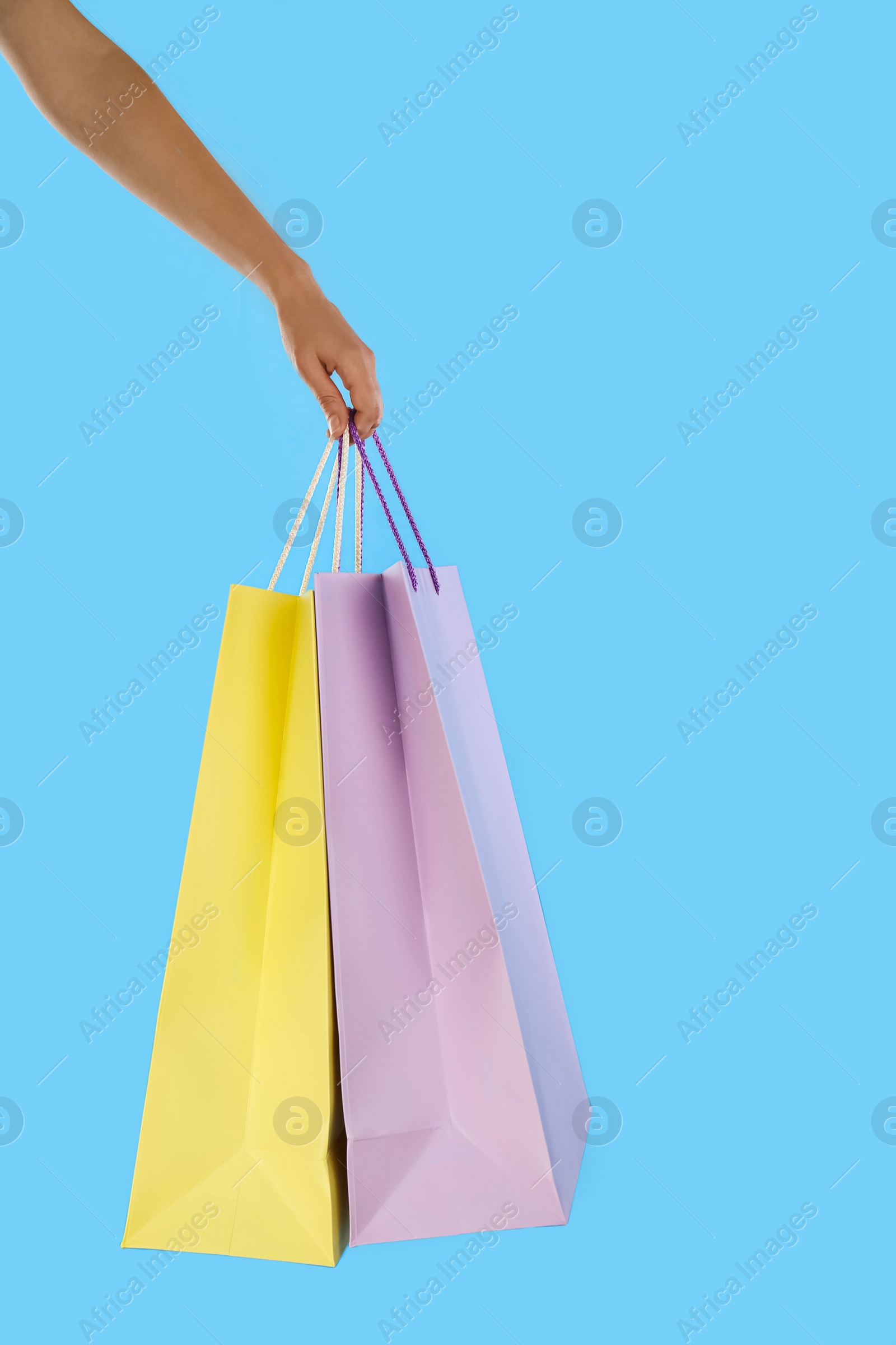 Photo of Woman with paper shopping bags on light blue background, closeup