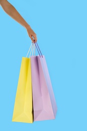 Woman with paper shopping bags on light blue background, closeup