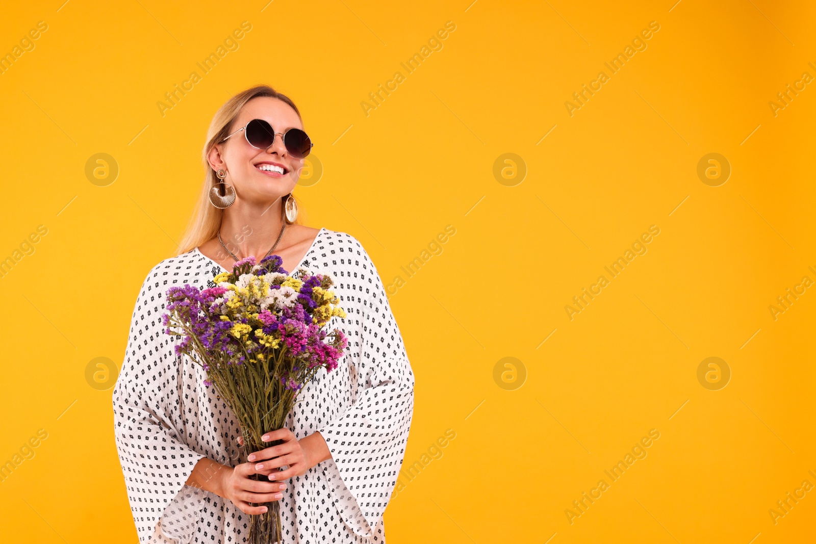 Photo of Portrait of smiling hippie woman with bouquet of flowers on yellow background. Space for text