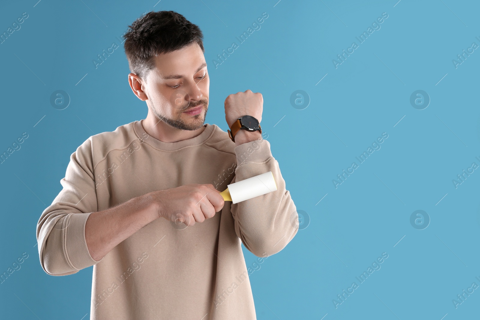 Photo of Man cleaning clothes with lint roller on light blue background. Space for text