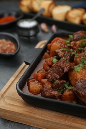 Photo of Delicious beef stew with carrots, parsley and potatoes on grey table, closeup