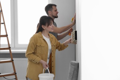 Woman and man hanging wallpaper in room