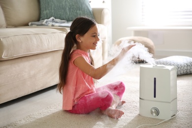 Photo of Little girl near modern air humidifier at home