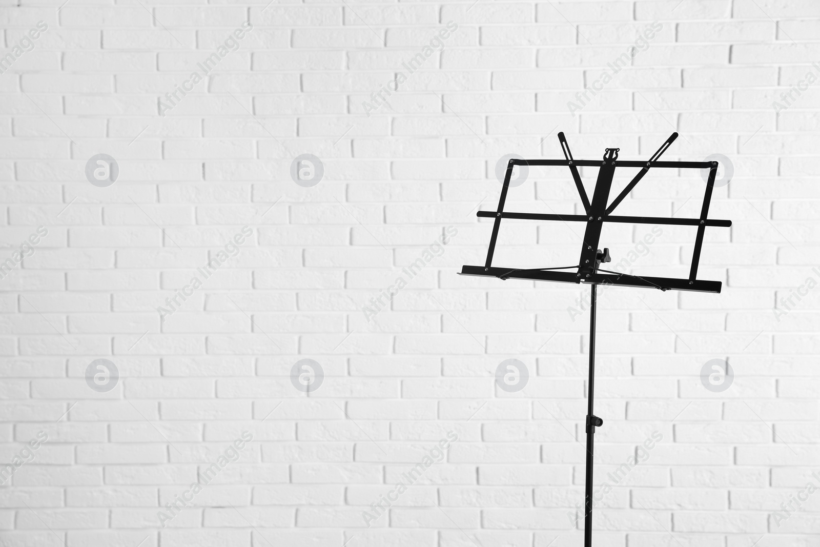 Photo of Empty music note stand near brick wall. Space for text