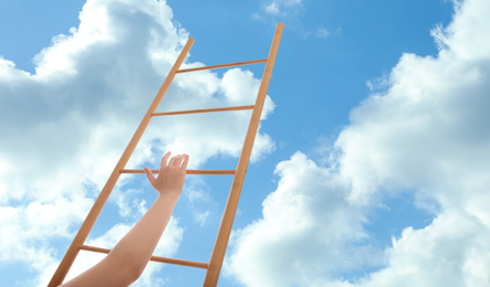 Woman climbing up wooden ladder against blue sky with clouds, closeup. Banner design 