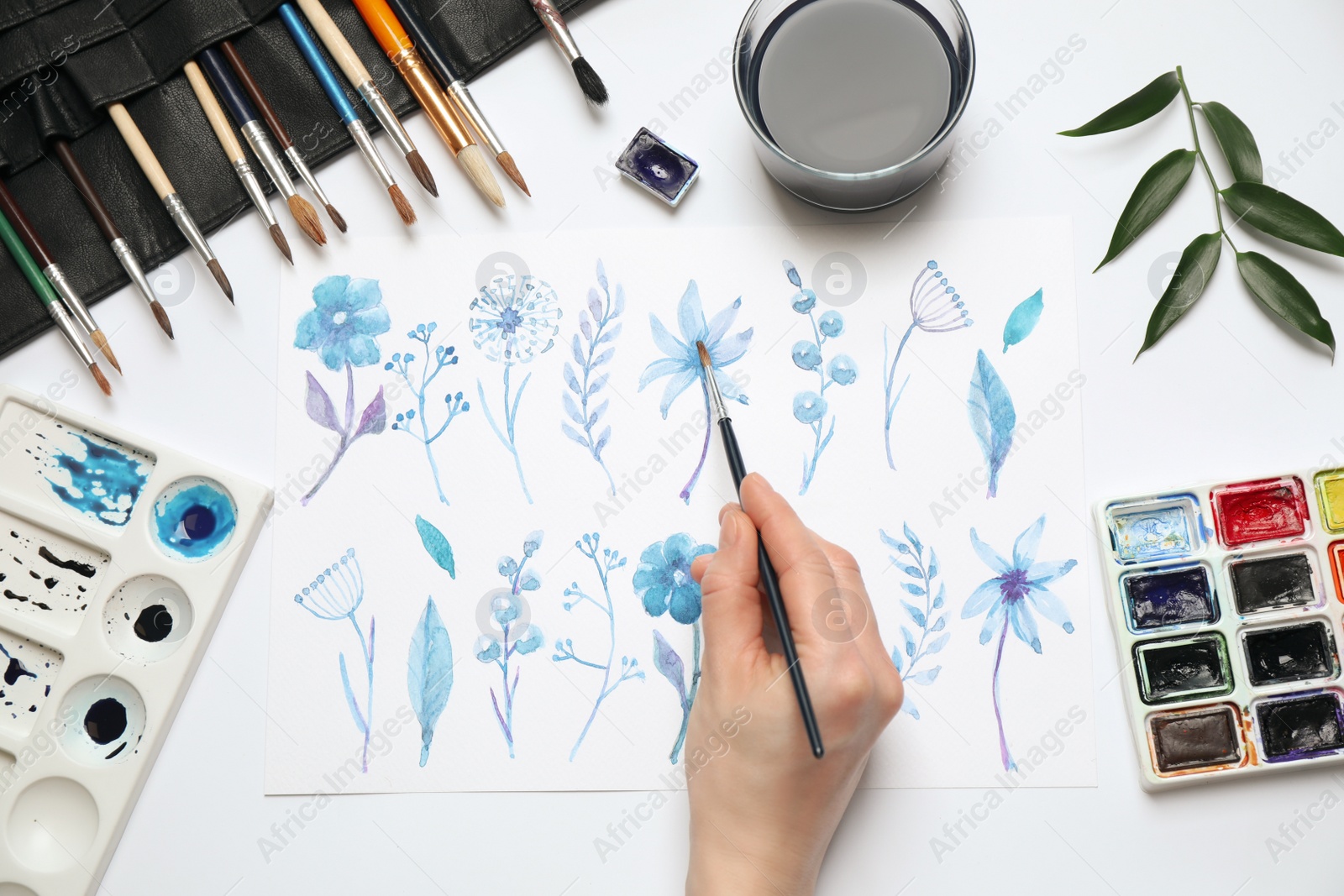 Photo of Woman painting flowers with watercolor at white table, top view