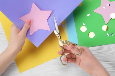 Photo of Woman cutting paper star with scissors at white wooden table, top view