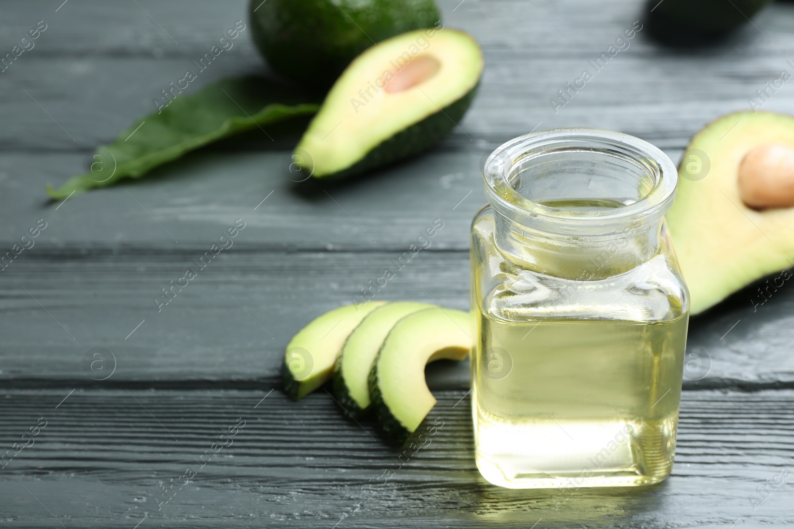 Photo of Jar of natural oil and avocados on grey wooden background. Space for text