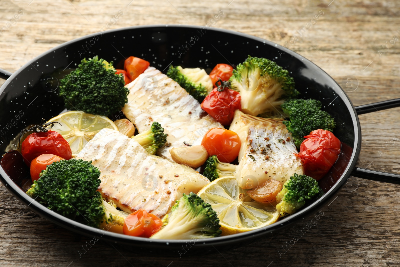 Photo of Tasty cod cooked with vegetables in frying pan on wooden table, closeup