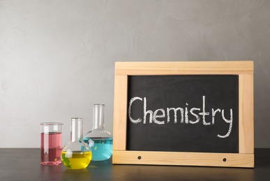 Laboratory glassware and chalkboard with word CHEMISTRY on table against grey background. Space for text