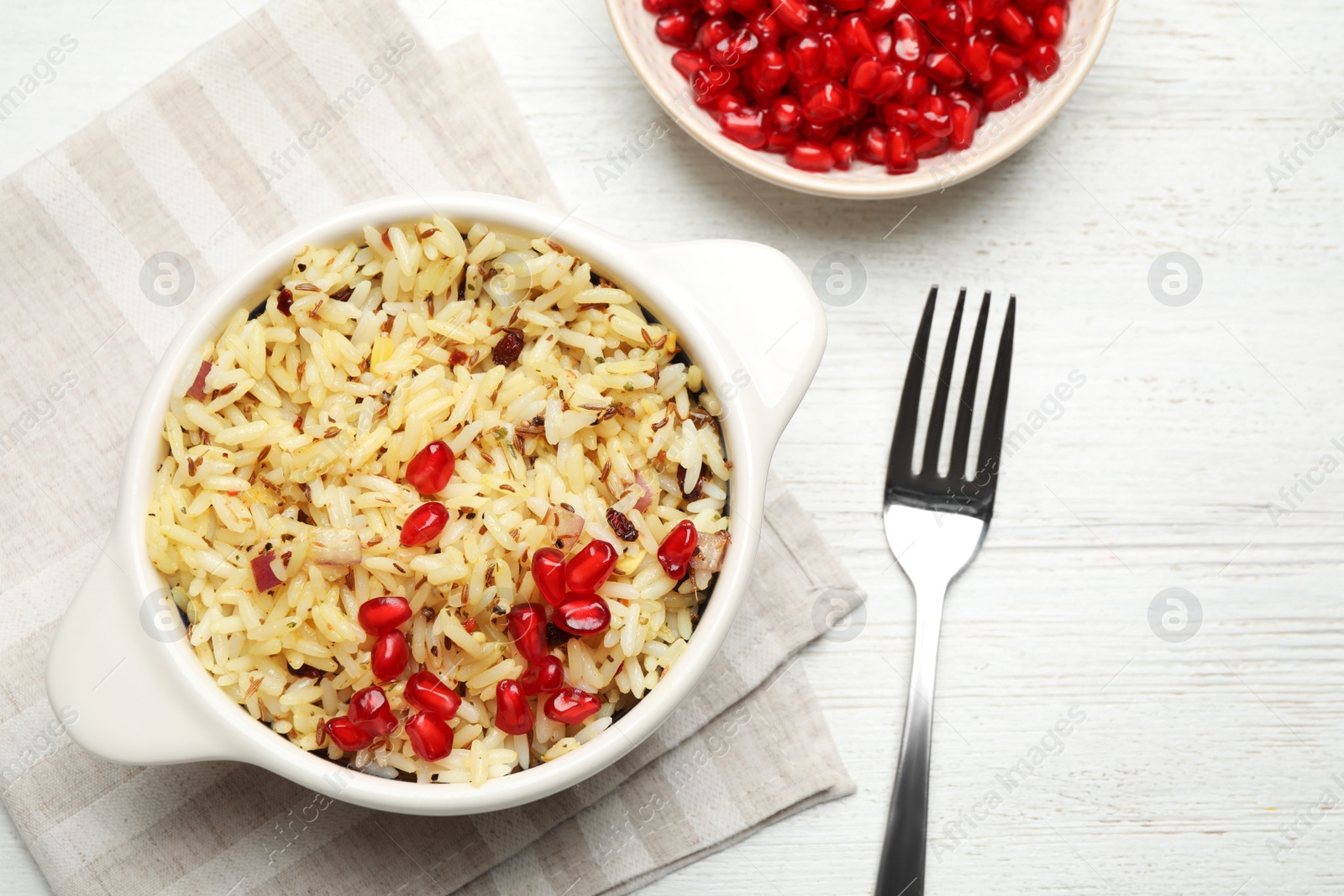 Photo of Tasty rice pilaf with pomegranate grains served on white wooden table, flat lay