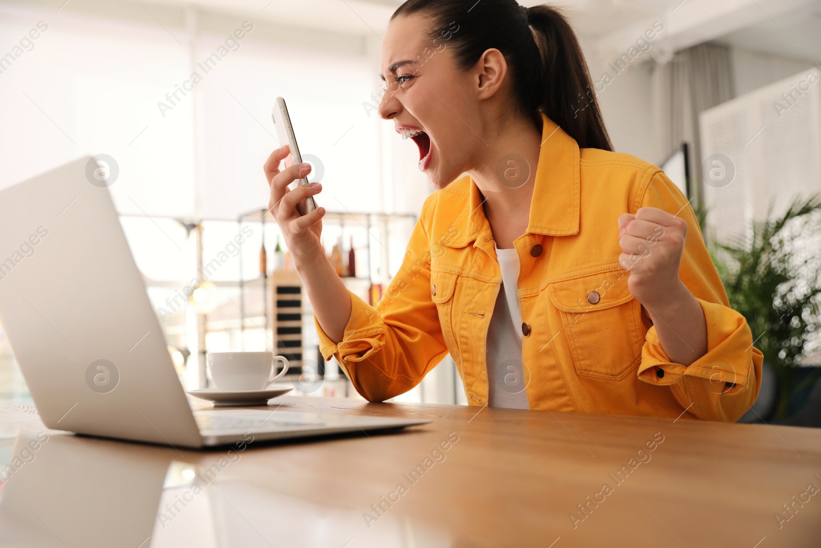 Photo of Emotional young woman with smartphone in office. Online hate concept