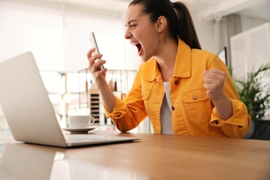 Emotional young woman with smartphone in office. Online hate concept