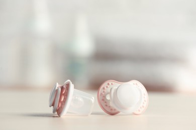 Photo of Baby pacifiers on beige table against blurred background, space for text