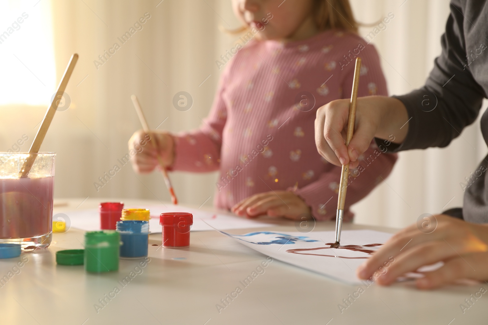 Photo of Little children drawing with brushes at light table indoors, selective focus