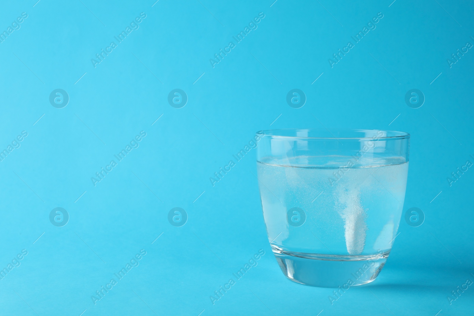 Photo of Glass of water with effervescent tablet on light blue background, space for text