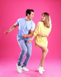 Beautiful young couple dancing on pink background