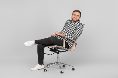 Photo of Young man sitting in comfortable office chair on grey background