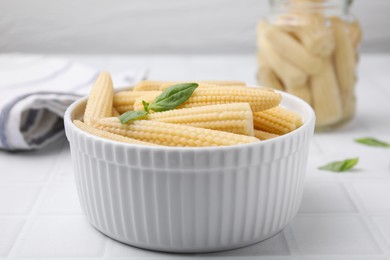 Photo of Canned baby corns with basil on white tiled table, closeup