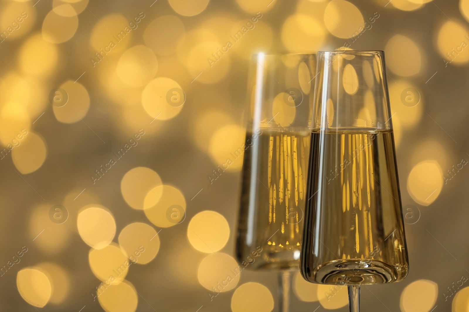 Photo of Glasses of fizzy champagne against blurred fairy lights, space for text