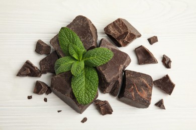 Tasty dark chocolate pieces with mint on white wooden table, flat lay