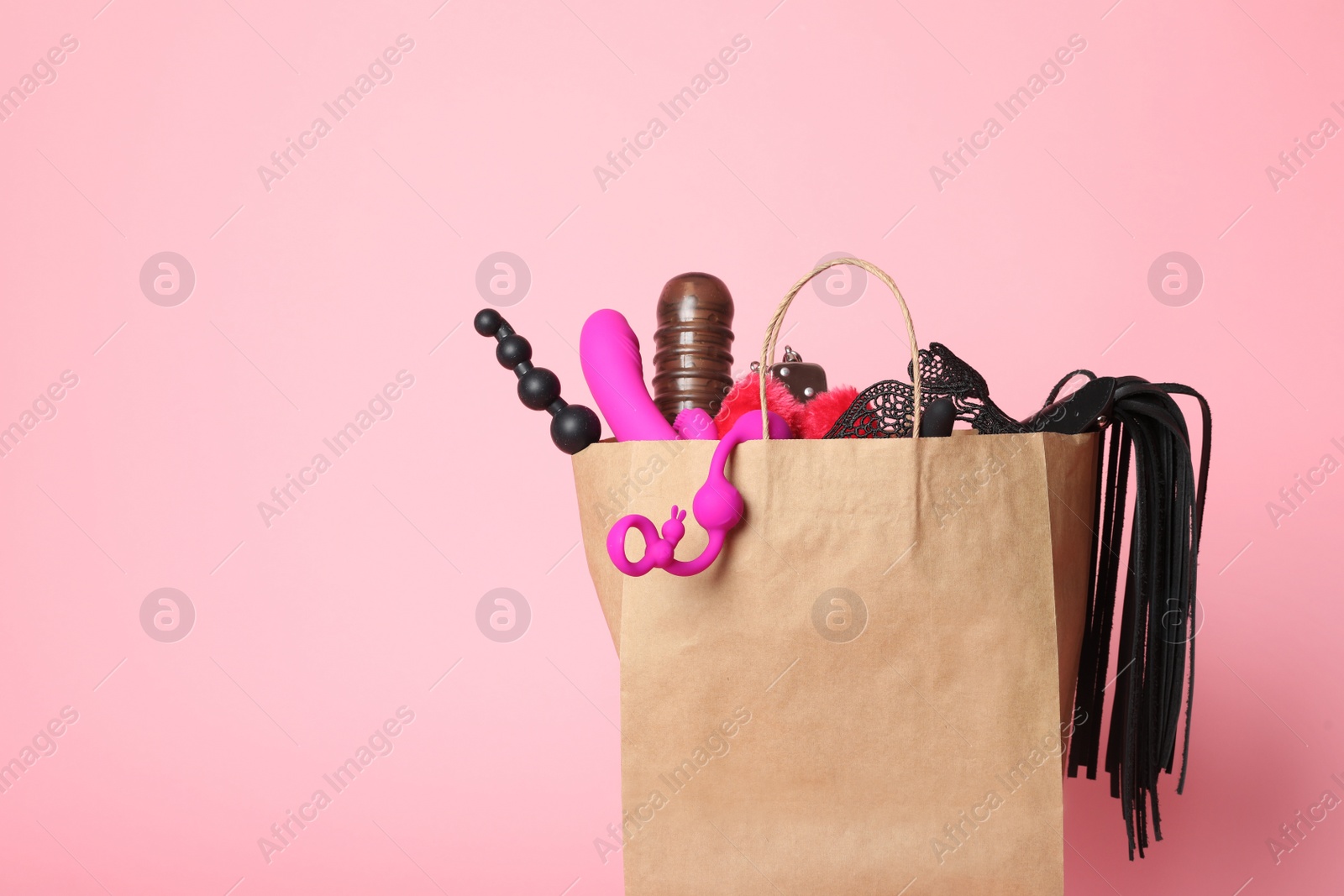 Photo of Paper shopping bag with different sex toys on pink background. Space for text