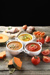 Photo of Tasty broth, cream soups in bowls and ingredients on old wooden table