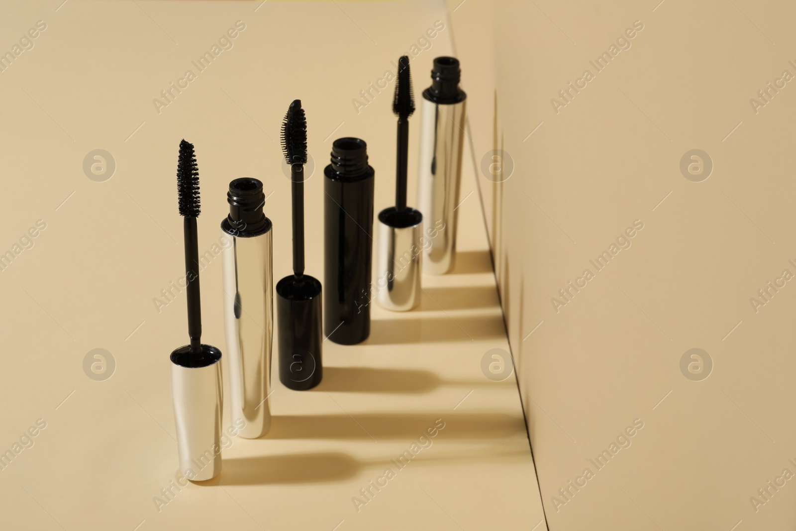 Photo of Row of different mascaras on beige background. Makeup product