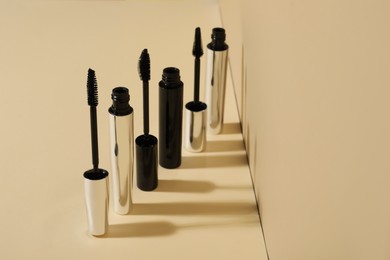 Photo of Row of different mascaras on beige background. Makeup product