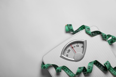 Photo of Weight loss concept. Scales and measuring tape on white background, top view. Space for text