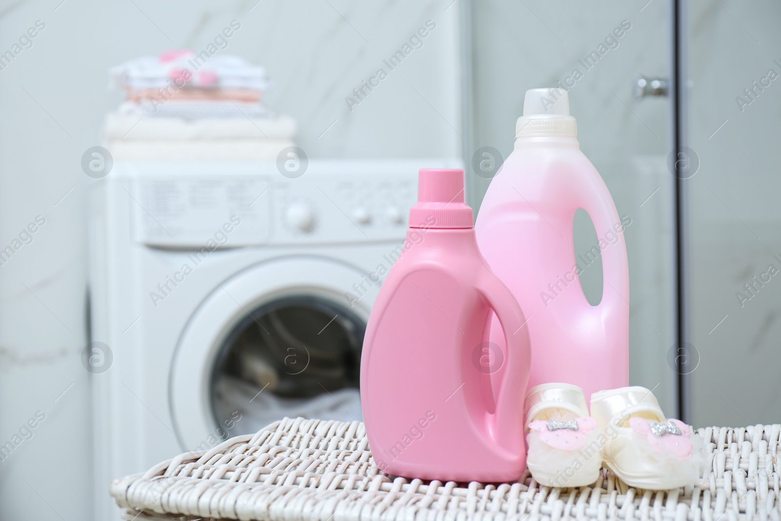 Photo of Bottles of detergent and children's boots on wicker basket in bathroom. Space for text