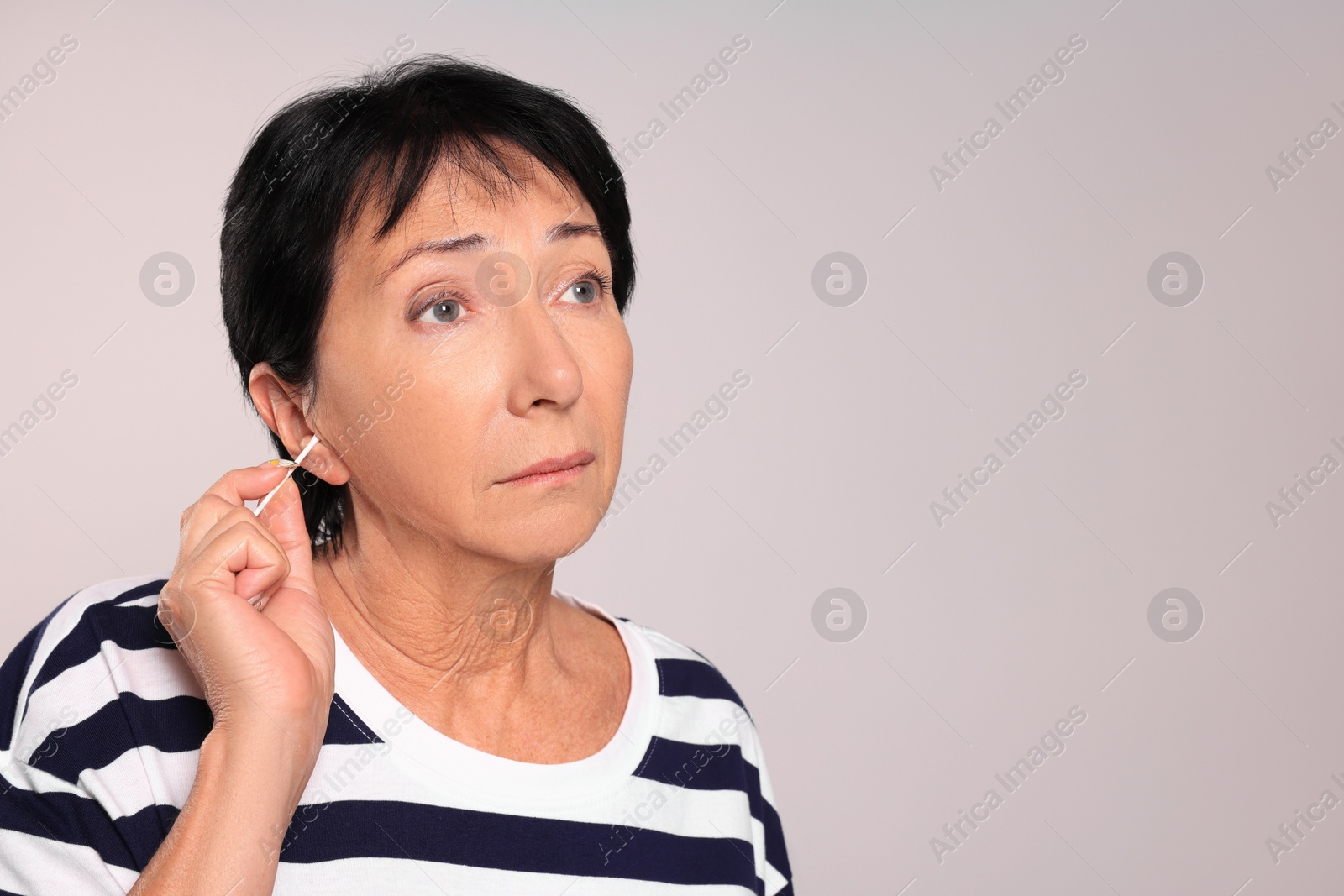 Photo of Senior woman cleaning ear with cotton swab on light grey background. Space for text