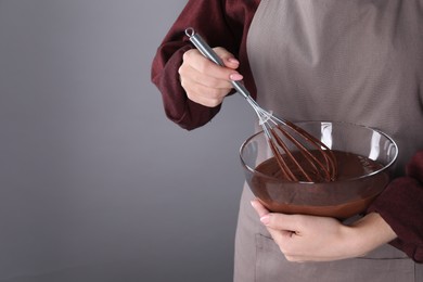 Woman with whisk making chocolate cream on grey background, closeup. Space for text