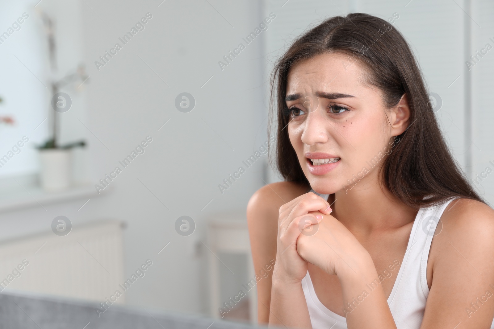 Photo of Young woman with eyelash loss problem looking in mirror indoors