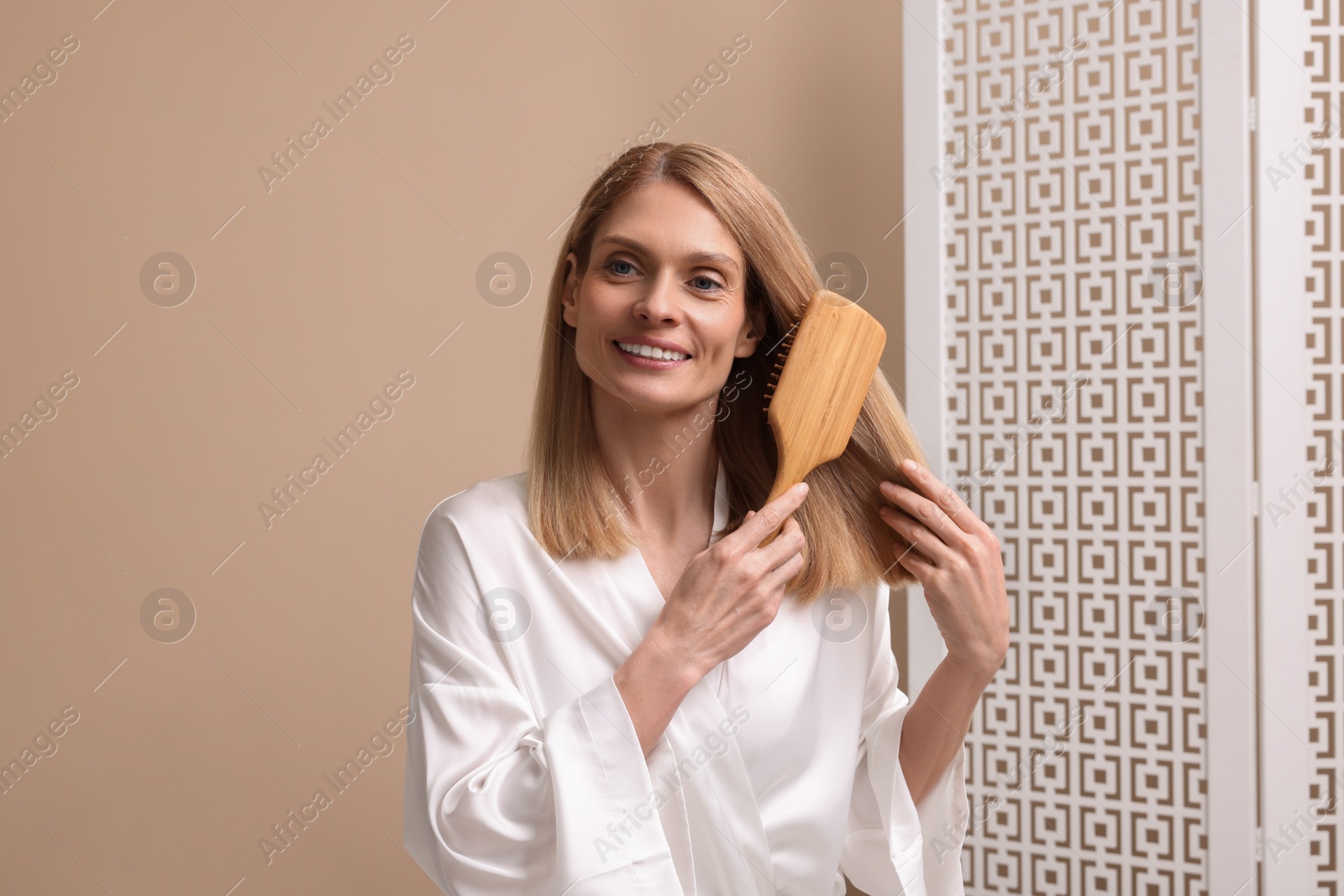 Photo of Beautiful woman in white robe brushing her hair indoors